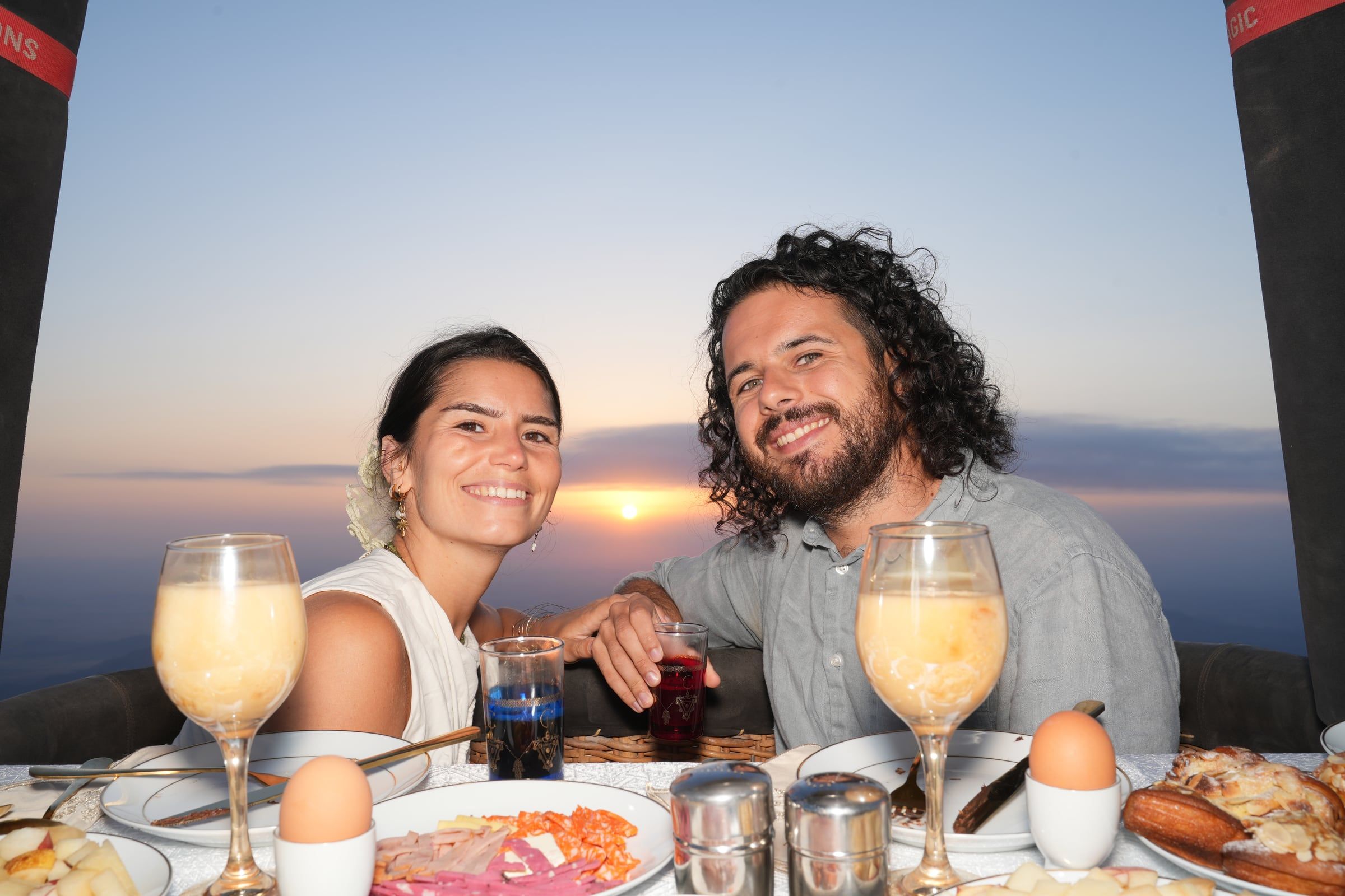 Couple smiling over breakfast in a hot-air balloon at sunrise