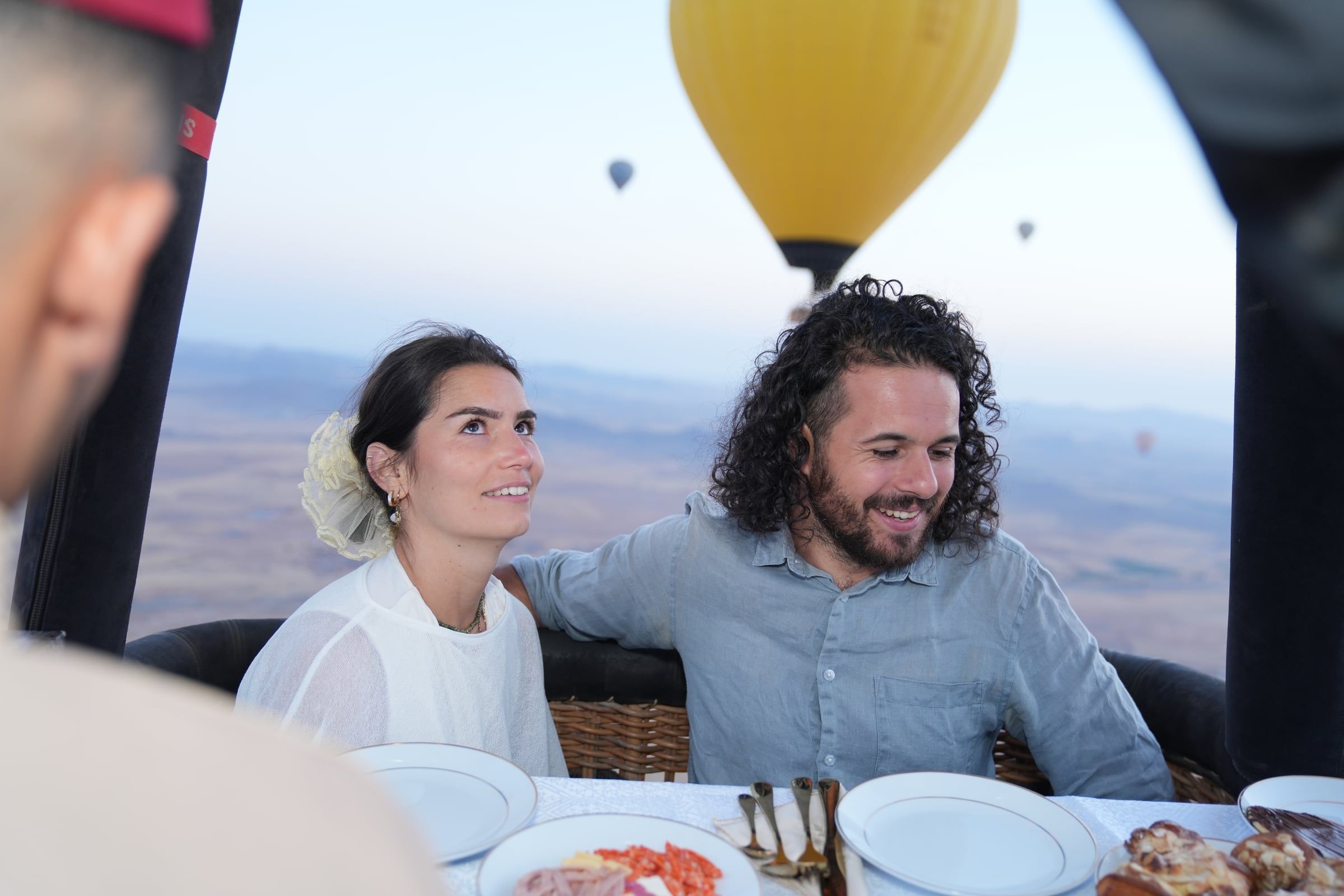 Couple smiling in a hot-air balloon basket over Marrakech, a yellow balloon behind them